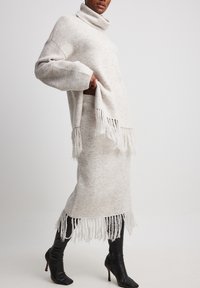 Hellgrauer Strickrollkragenpullover mit Fransen am Saum, kombiniert mit einem passenden Rock und ergänzt durch schwarze kniehohe High Heels.