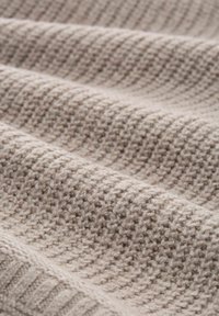 Beige knitted fabric with a textured pattern, featuring alternating rows of tight and loose stitches, creating a soft, warm appearance.