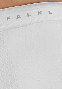 Collants blancs en tissu avec une taille côtelée arborant le texte gris "FALKE." La matière a une texture lisse avec un motif subtil.