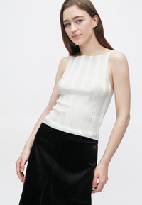 Bijela majica bez rukava s okomitim rebrastim uzorkom, valovitim izrezom i uskim krojem, u kombinaciji s crnom suknjom A-kroja od umjetne kože s uzorkom reptila.