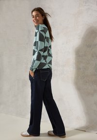 Maglione a scacchi blu chiaro e grigio scuro con maniche lunghe, abbinato a jeans a gamba larga blu scuro e sneakers bianche.