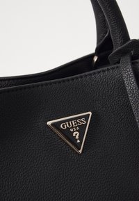 Sort håndtaske i imiteret læder med tekstureret overflade, med trekantet metal-logo i guld og sort på forsiden.