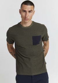 Camiseta de manga corta de color verde oliva con un patrón de rayas en azul marino oscuro y un bolsillo en el pecho. Cuello redondo acanalado y textura suave.