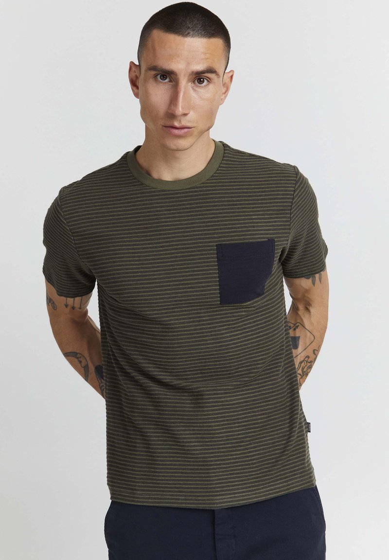 Camiseta de manga corta de color verde oliva con un patrón de rayas en azul marino oscuro y un bolsillo en el pecho. Cuello redondo acanalado y textura suave.