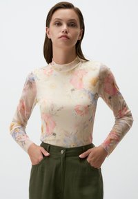 Top floreale a maniche lunghe in tessuto trasparente. Colori pastello morbidi con fiori rosa, blu e gialli. Collo alto con design aderente e texture liscia.