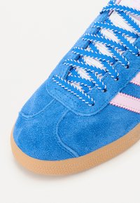 Sneaker blu scamosciato con accenti rosa, lacci bianchi e una suola in gomma testurizzata. Presenta una punta arrotondata e dettagli di cucitura unici.