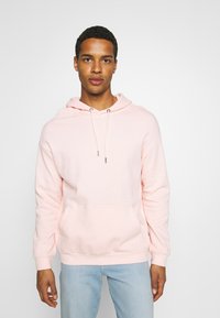 Lys rosa hettegenser med kengurulomme, snor i hetta, myk stoff, ribbestrikkede mansjetter og nederkant, sammen med lyseblå jeans.