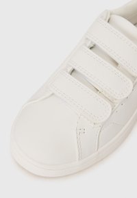 Hvid syntetisk sko med tre velcro remme, rund tå, glat tekstur og syede detaljer. Lidt forhøjet gummisål.