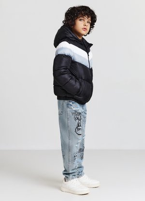 Giacca nera, imbottita, con strisce orizzontali azzurro chiaro e bianche, abbinata a jeans azzurri strappati con stampe grafiche nere e sneaker bianche.