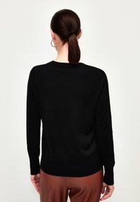 Svart stickad tröja med långa ärmar, rund halsringning och ribbad nederkant. Slät textur med minimala detaljer, bärs med bruna byxor.