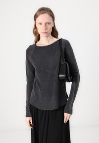 Ilga rankovė, tamsiai pilka, medvilnės ir sintetinių pluoštų mišinys, su apvaliu iškirpimu ir lenktu hemu. Pora su juoda krepšine ant peties. Paprasta tekstūra, kasdienis dizainas.