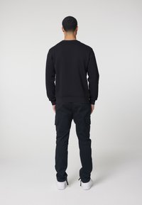 Black sweatshirt with ribbed neckline and cuffs, paired with dark cargo pants featuring side pockets, and white sneakers.
