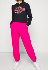 Black cropped hoodie with red and white Adidas logo; pink ribbed joggers with elastic waistband; paired with white sneakers.