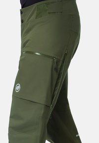 Pantalons de ski texturés vert olive, avec une poche zippée, des fermetures à bouton et un patch logo. Présente des coutures renforcées et une coupe ajustée.