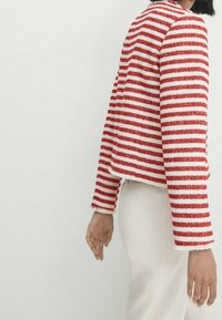 Veste texturée rayée rouge et blanche au design court, avec des manches longues et un col rond. Associée à un bas de couleur claire.