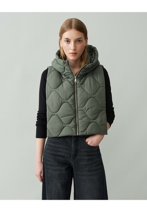 Gequilted groene puffer vest met een capuchon, achterrits en een gestructureerd patroon; gedragen over een zwart shirt met lange mouwen en gecombineerd met donkere spijkerbroek.