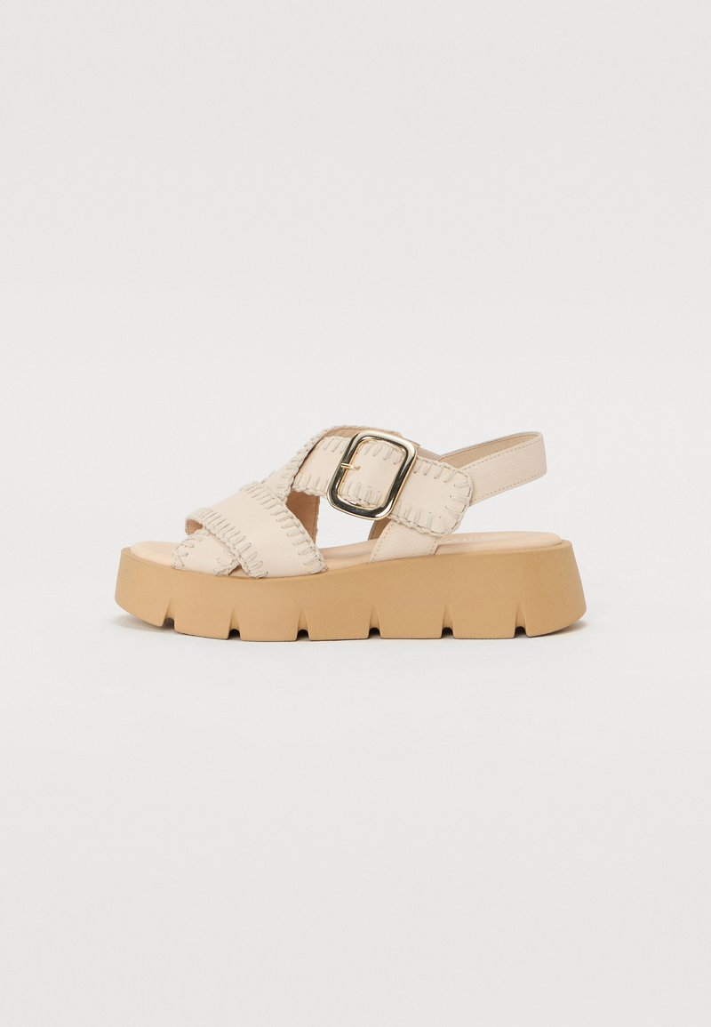 Sandali platform beige con cinturini incrociati, dotati di una fibbia dorata e cuciture testurizzate; suola in gomma spessa e rigida per una maggiore stabilità.