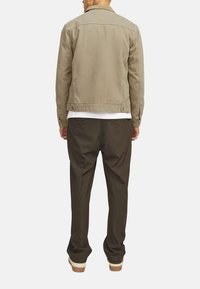 Veste en denim khaki au design structuré, assortie à un pantalon brun ample et une chemise blanche. Couture visible et détails matériels subtils.