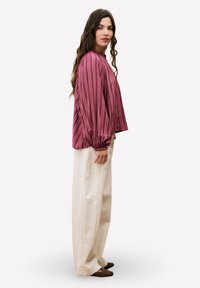 Blouse à manches longues rayée bordeaux avec un col rond et des poignets froncés, associée à un pantalon large crème et des chaussures sombres.