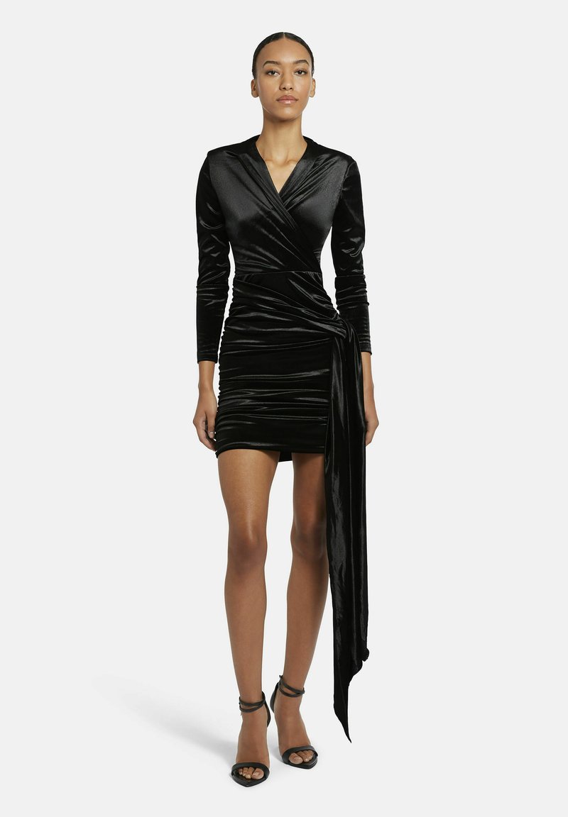 Schwarzes Samtwickelkleid mit langen Ärmeln, das einen tiefen V-Ausschnitt, geraffte Textur und einen angenähten, drapierten Gürtelakzent aufweist.