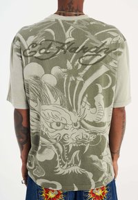 Olivgrön t-shirt med ett detaljerat drakmotiv och molnmönster på ryggen. Kortärmad med en avslappnad passform. Ed Hardy-logotyp ingår.