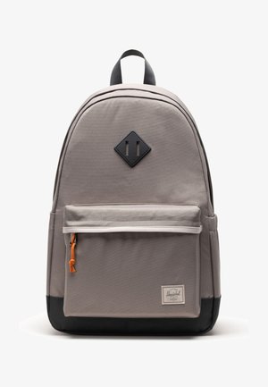 Grauer Stoffrucksack mit einem rautenförmigen Logo, schwarzen Akzenten und einer vorderen Reißverschlusstasche mit einem orangefarbenen Zipper. Glatte Textur.