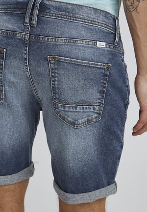 Shorts en denim bleu délavé avec revers, dotés de deux poches arrière et de surpiqûres contrastantes le long des bords et des coutures des poches.