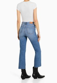 Světle modré krátké džíny s neupraveným lemem, vysokým pasem a zadními kapsami, doplněné těsně padným bílým topem a černými kotníkovými botami.