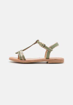 Grønne syntetiske sandaler med stropper og T-bar design, der har gyldne detaljer og en tan flad sål. Justerbar ankelspænde for en sikker pasform.