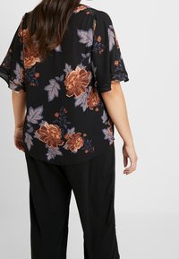 Blusa nera a fiori con maniche corte, caratterizzata da grandi rose arancioni e viola e foglie verdi. Tessuto leggero e fluido con un orlo curvo.
