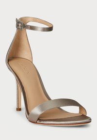 Sandal de salto alto em cetim metálico prateado, com uma tira fina no tornozelo, bico aberto e um elegante salto aguçado. Textura suave com detalhes mínimos.