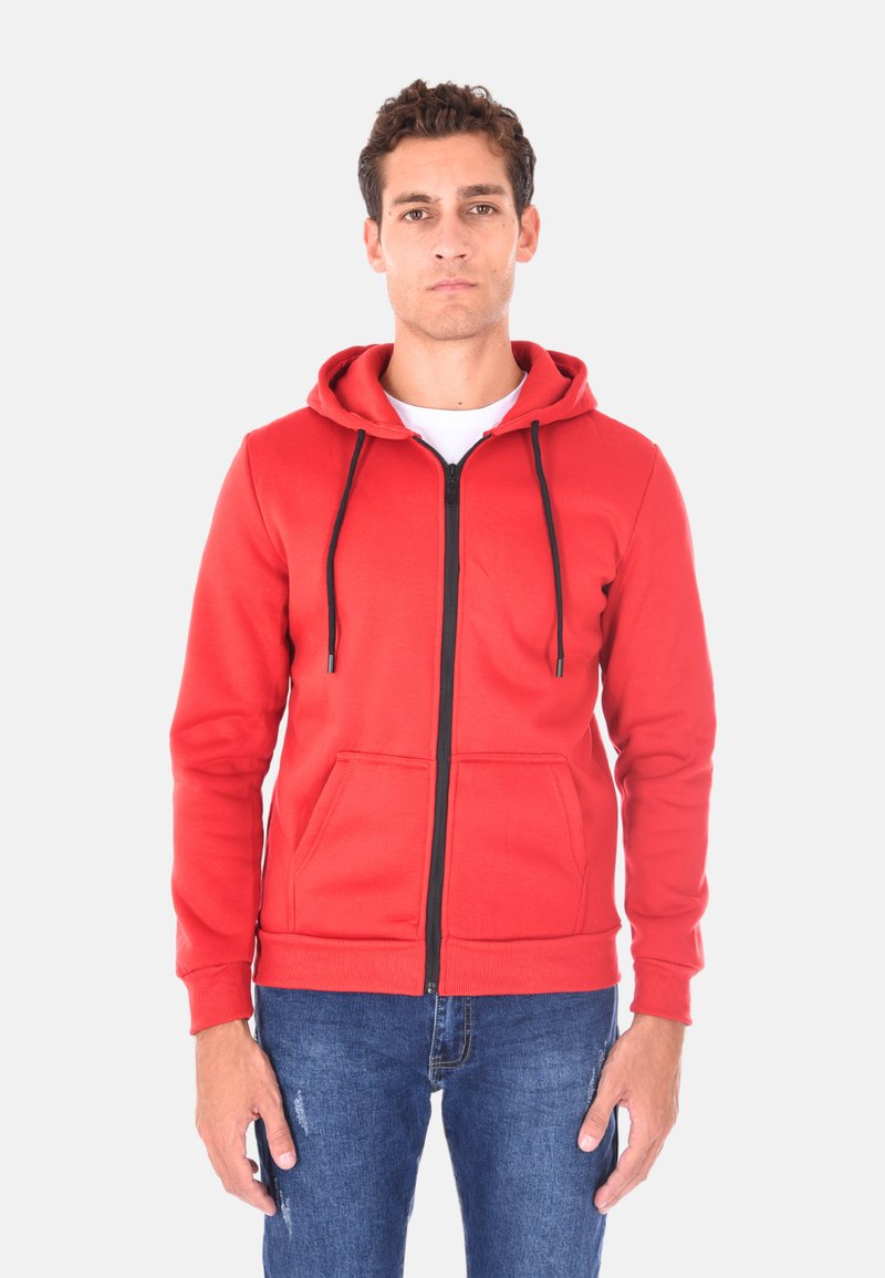 Felpa rossa con zip e cappuccio regolabile, dotata di due tasche frontali e una cerniera nera. Texture liscia; indossata sopra una maglietta bianca e jeans blu.