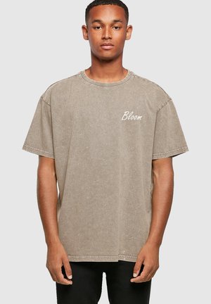 Overdimensioneret beige T-shirt med rund hals og korte ærmer. Har ordet "Bloom" broderet i hvidt i venstre brystområde.