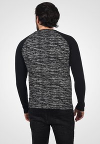 Langermet skjorte med et svart og grått melert mønster på kroppen og ensfargede svarte ermer. Stoffet ser mykt ut med en vanlig passform.