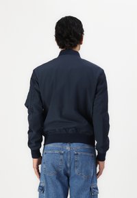 Mørkeblå bomberjakke med ribbestrikket krage og mansjetter, glatt stoff, sidelommer og innsvinget midje, kombinert med lyseblå cargo-jeans.