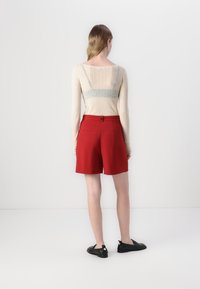 Shorts rouges ajustés avec deux poches arrière, associés à un haut beige clair à manches longues côtelé, présentant un détail rayé transparent.