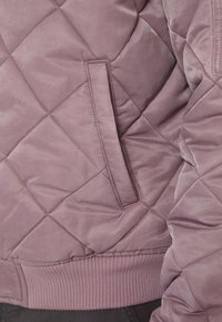Quilted pink jacket featuring a side pocket, ribbed hem, and smooth texture, highlighting diamond stitching in a subtle sheen.