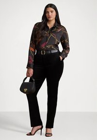 Black velvet pants with a fitted design, paired with a black and colorful patterned blouse featuring chains, and a small black handbag.