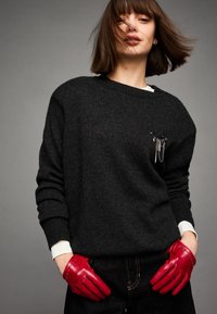 Fekete kötött pulóver kerek nyakkiv�ágással, díszes fém lánc részlettel. Kiegészítve sima vörös bőr kesztyűvel és sötét farmernadrággal.