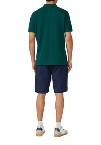 Grünes Polo-Shirt mit kurzen Ärmeln und strukturiertem Finish, kombiniert mit marineblauen Shorts. Dazu gehören cremefarbene Sneakers mit dunkelblauen Akzenten.
