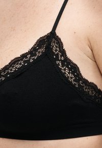 Κοντινό πλάνο ενός μαύρου τιράντα και κυπέλλου στράπλες σουτιέν με δαντέλα στον άνω θώρακα και στην περιοχή του ώμου ενός ατόμου με ανοιχτόχρωμο δέρμα.