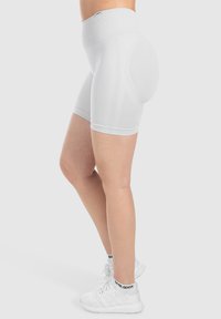 Pantaloni corti bianchi a vita alta in compressione con texture a coste, design aderente e lunghezza fino a metà coscia, abbinati a scarpe da ginnastica bianche.