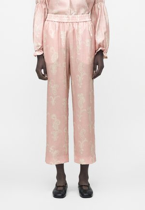 Modellen har højttaljede rosa bukser med beige paisley-mønster og elastisk talje på, kombineret med matchende langærmet top og sorte flade sko.