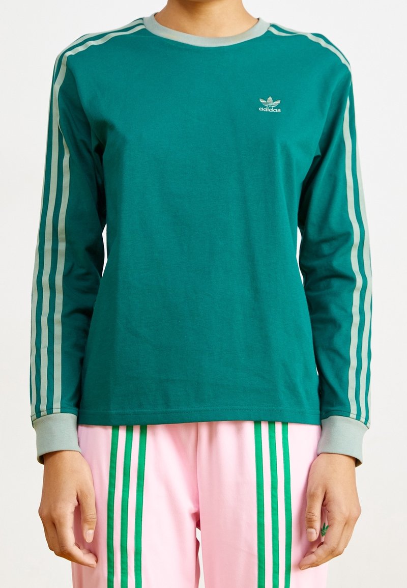Grön långärmad skjorta med grå ribbad krage och manschetter, har tre grå ränder längs ärmarna, inkluderar liten vit Adidas-logotyp på bröstet.