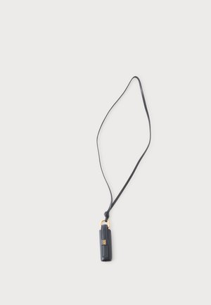 Soporte para colgante de cuero negro con un anillo dorado y una correa larga sobre un fondo claro y liso.