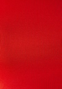 Rød ribbestrikket stoff med en glatt tekstur og vertikale linjer, som utviser en livlig farge som forsterker visuell dybde og dimensjon.