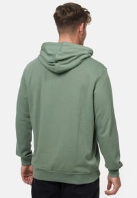 Grüne Kapuzenjacke mit weicher Textur, ausgestattet mit einer Kordelzug-Kapuze, langen Ärmeln und gerippten Bündchen sowie Saum. Einfaches, klares Design.