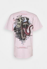 Camiseta de algodón rosa con un gráfico detallado de un cráneo y la boca de Venom con una lengua larga y texturizada, contorneada en negro y colores pastel.