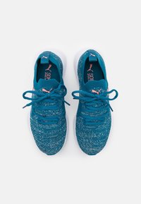 Zapatillas deportivas de punto azules con un patrón texturizado, suelas de goma blanca y acentos en rosa contrastante en el logo y los cordones.