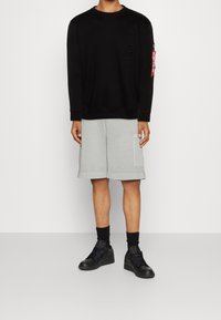 Felpa nera con logo in rilievo, pantaloni corti grigi chiari con tasche laterali e sneakers nere. Look informale con una vestibilità comoda.